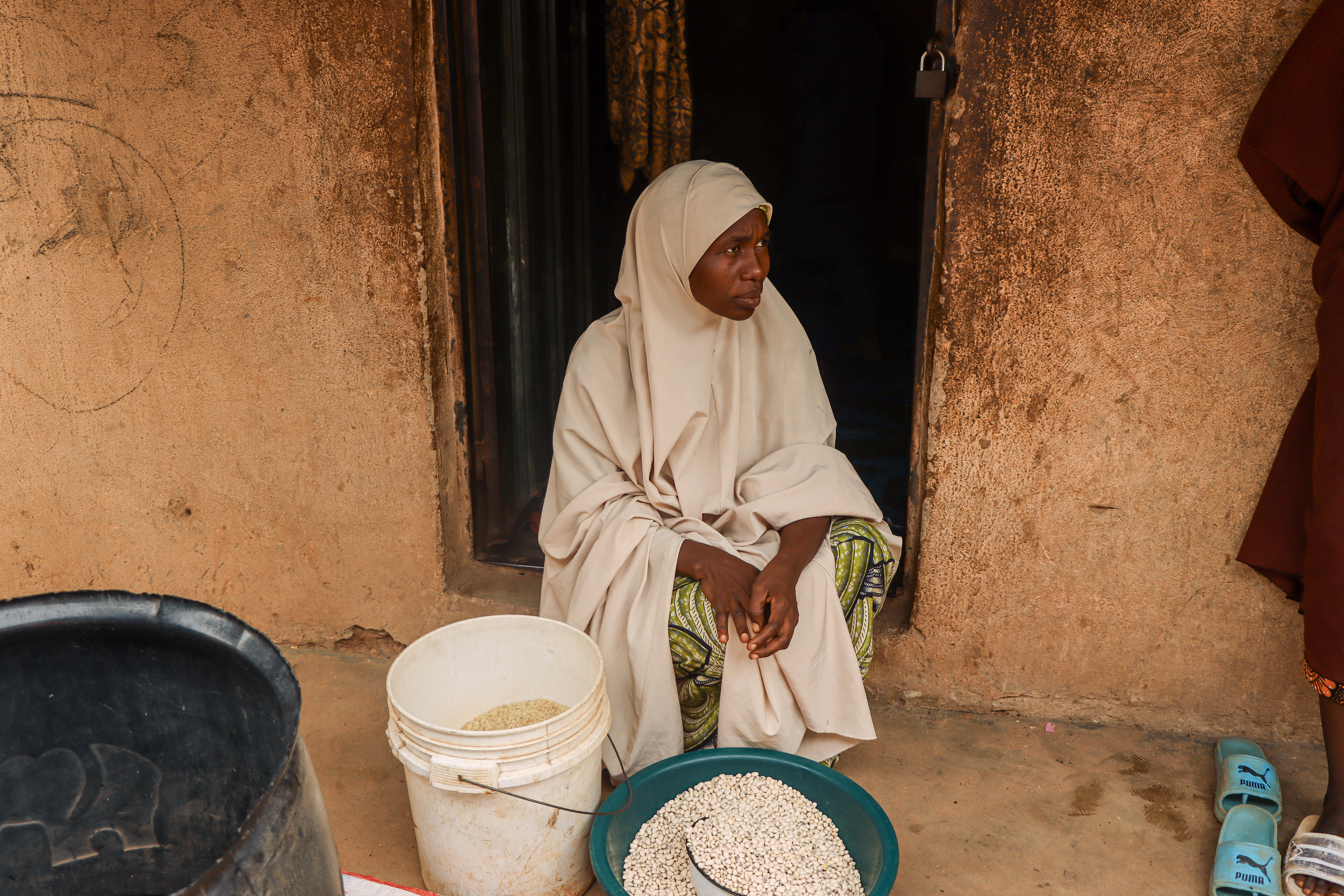 Maimuna sitting in front of her apartment with some of her food items displayed in front of her 